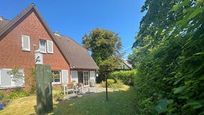 A brick house with a sloped roof, a small garden with a wooden fence, and a tree. - Strandgut - Half of a house in the center of Zingst (Zingst)