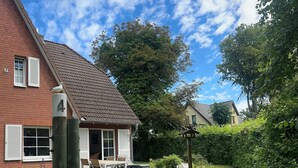 A house with a brick exterior, a tiled roof, and a garden with a lawn and a wooden post. - Strandgut - Half of a house in the center of Zingst (Zingst)