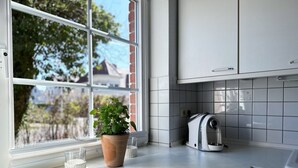 A kitchen with a large window, a potted plant, a kettle, and a tiled backsplash. - Strandgut - Half of a house in the center of Zingst (Zingst)