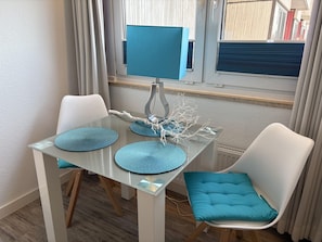 A dining area with a glass table, white chairs, and blue cushions.