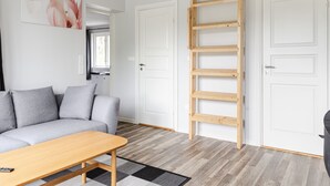 A modern living room with a grey sofa, a wooden table, and a wooden ladder leading to a loft. - Jönsamåla by Interhome (Ryd)