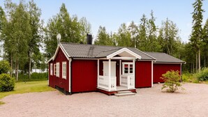 A red wooden cabin with a white porch, surrounded by a gravel driveway and a forested area. - Jönsamåla by Interhome (Ryd)