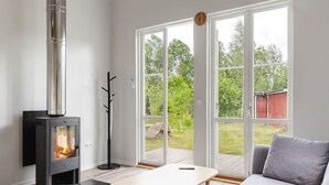 A modern living room with a wood-burning stove, a sofa, a coffee table, and large windows offering a view of the outdoors. - Jönsamåla by Interhome (Ryd)