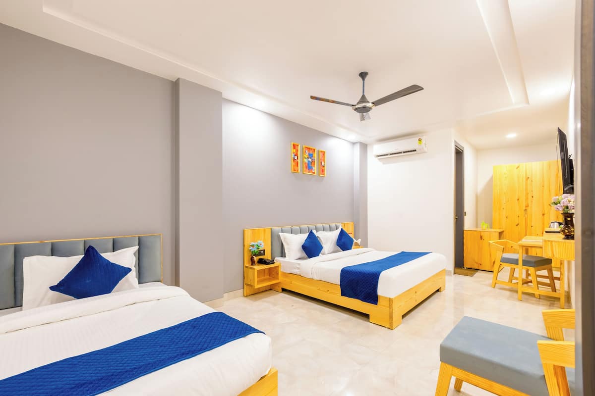 A modern hotel room with two beds, a ceiling fan, a wooden desk, and a small seating area.