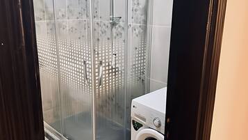 A modern bathroom with a glass shower enclosure, a washing machine, and tiled walls.