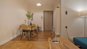 A modern dining area with a wooden herringbone floor, a round table with chairs, a vase with a plant, and a door in the background. - Historic Boutique Apartment in Artists' Kipseli (Athina)