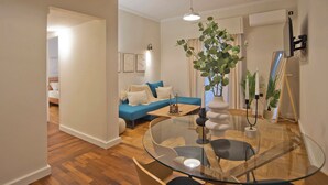 A modern living room with a glass coffee table, a blue sofa, and a large plant. - Historic Boutique Apartment in Artists' Kipseli (Athina)