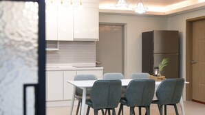 Una cocina moderna con armarios blancos, un refrigerador de acero inoxidable y una zona de comedor con mesa blanca y sillas grises.