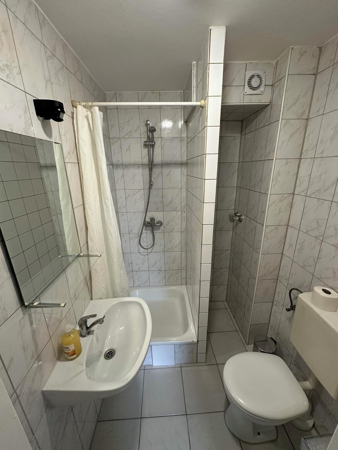 Une petite salle de bain avec une douche, des toilettes, un lavabo et un miroir.