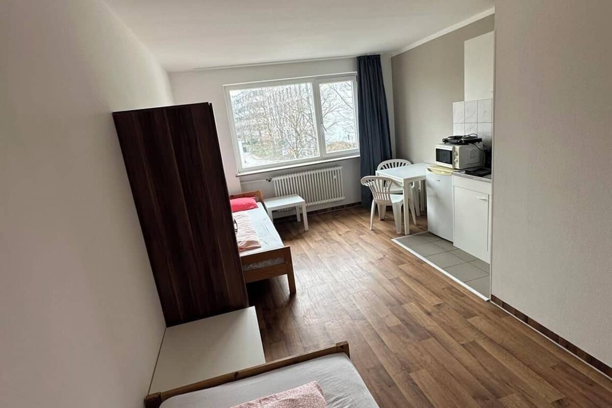 Habitación pequeña con cama, escritorio y kitchenette.