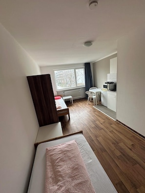 Ein kleines Zimmer mit Bett, Schreibtisch und einer Küchenzeile.
