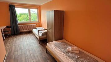 Habitación individual con piso de madera, una ventana con cortinas, un radiador y un armario.