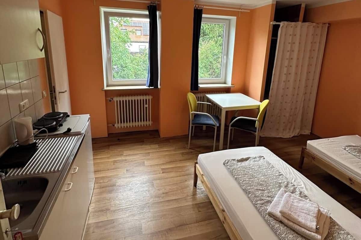 Habitación compacta con kitchenette, dos camas individuales, una mesita y dos ventanas.
