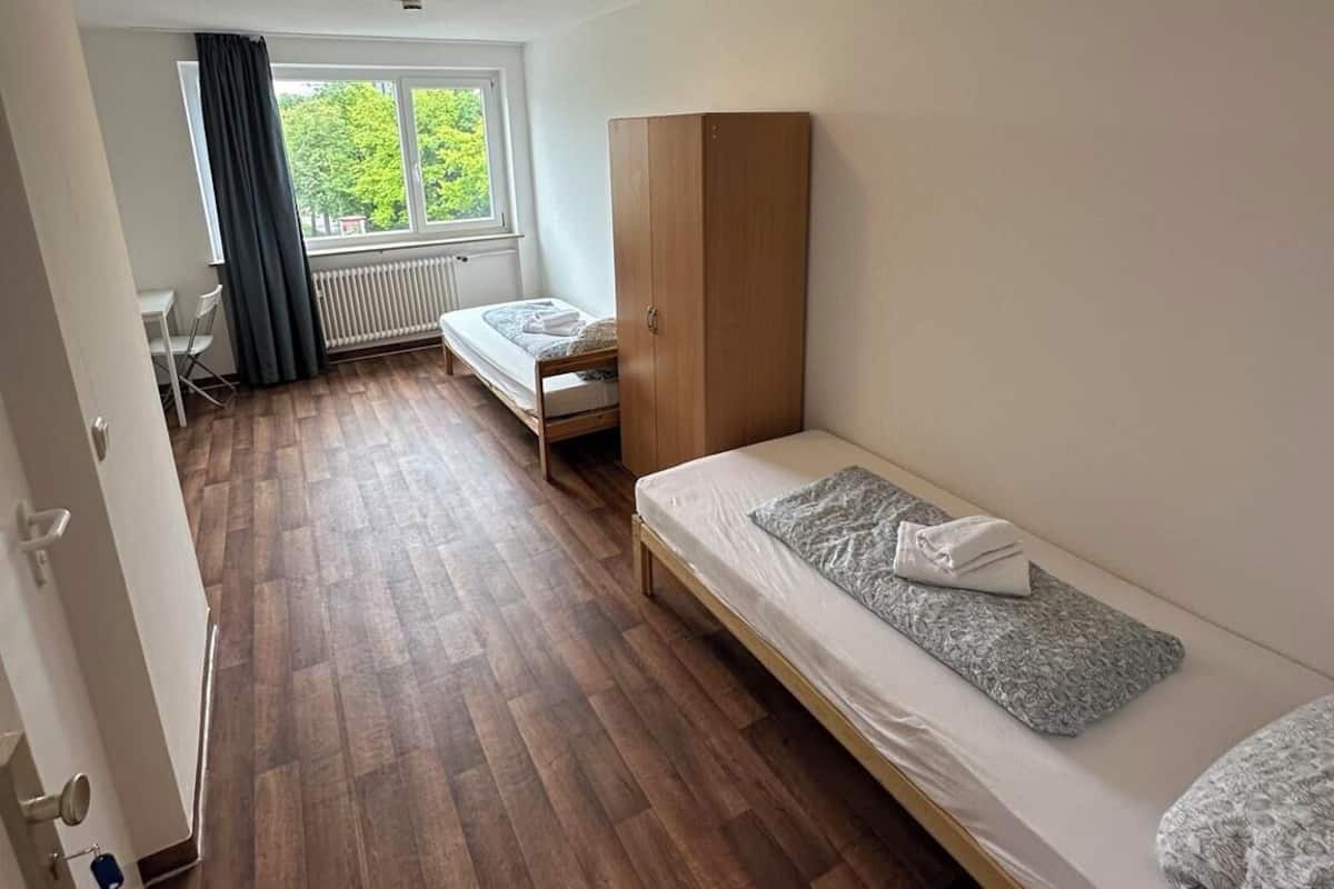 Un dormitorio con suelo de madera, una cama individual, un armario, un radiador y una ventana con vistas a zonas verdes.