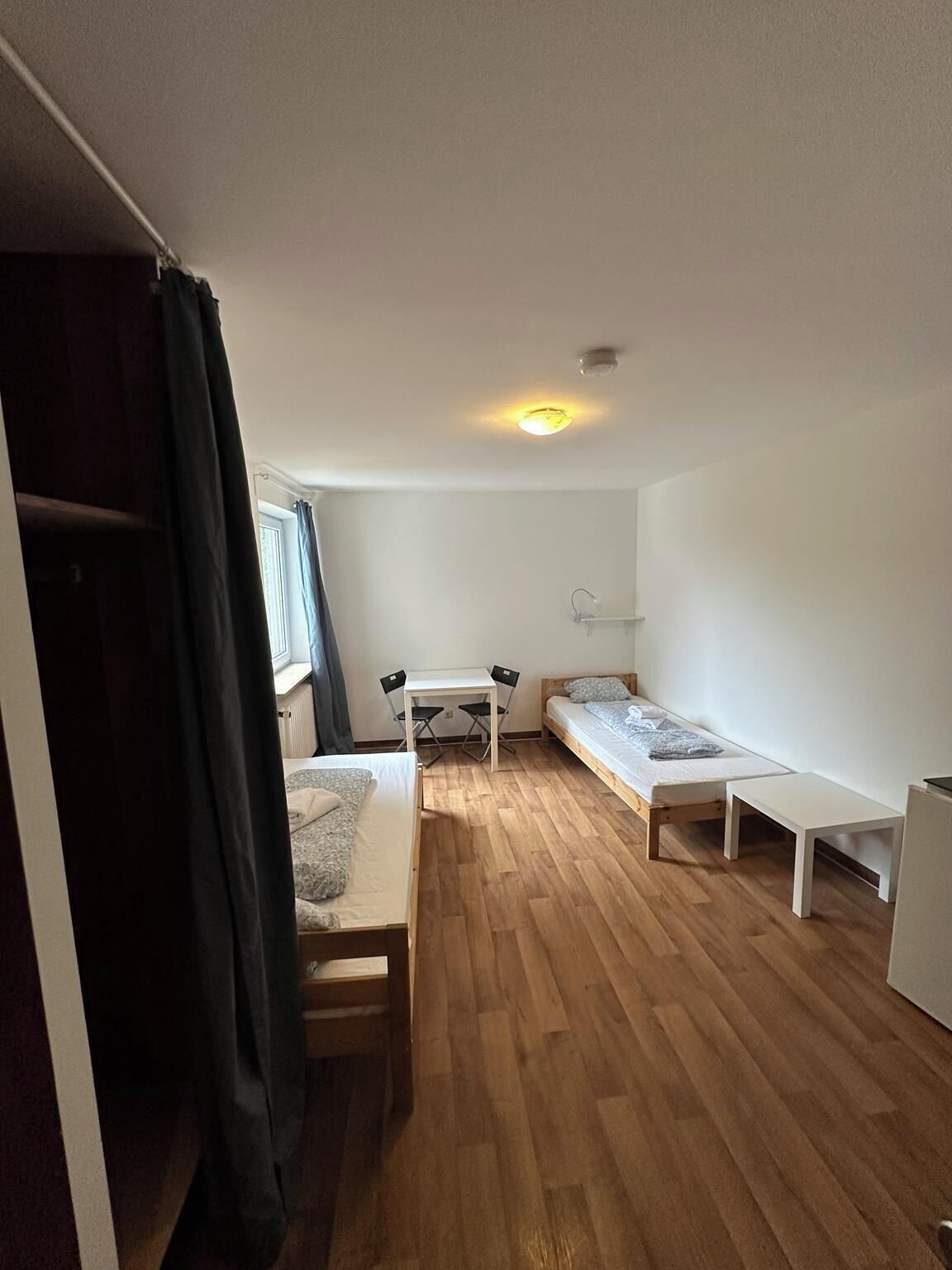 Ein kleiner, gut beleuchteter Raum mit einem Bett, einem Schreibtisch und einem Stuhl.