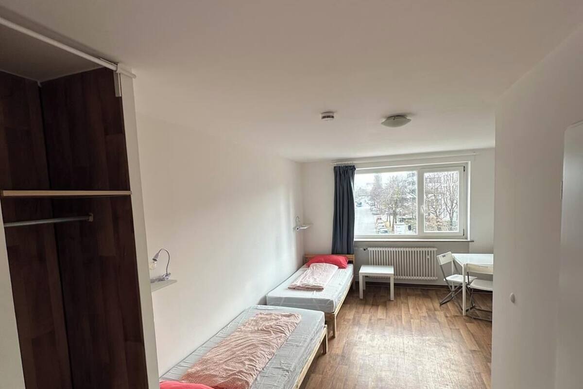 Un dormitorio con dos camas individuales, un escritorio, una silla y un radiador cerca de una ventana.