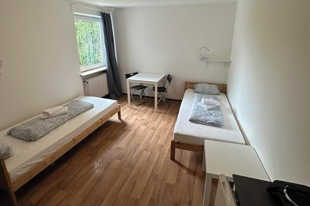 Una habitación pequeña y luminosa con dos camas individuales, una mesita y un radiador.