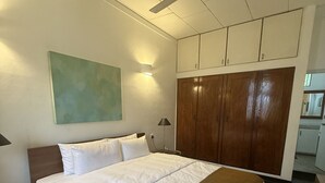 Une chambre d’hôtel avec un lit, une armoire, un ventilateur de plafond et un tableau au mur.