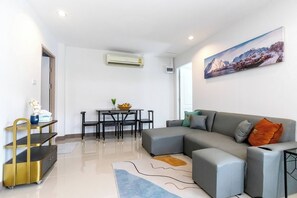 Un salon moderne avec un canapé d’angle gris, une table à manger avec des chaises, une étagère à cadre doré et un tableau accroché au mur.