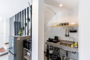 Une cuisine compacte équipée d’un réfrigérateur encastré, d’un four à micro-ondes et d’un évier surmonté d’une étagère en bois.
