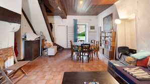A cozy room with a wooden ceiling, a dining table with chairs, a sofa, a bookshelf, and a window with curtains. - Domaine de La Contie – 17th-Century Chartreuse in the Heart of 20 Hectares of Nature (Issac)