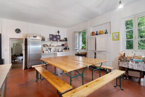 Une cuisine avec une grande table en bois, des bancs, un réfrig érateur et une fenêtre donnant sur un paysage verdoyant.