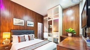 Een hotelkamer met een groot bed, houten lambrisering, een bureau, een televisie en een kamerplant.