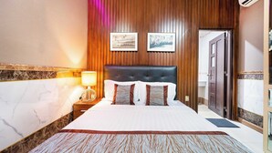 Een hotelkamer met een groot bed, houten paneelwanden, twee ingelijste foto's, een nachtkastje met een lamp en een deur.