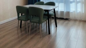 Un coin repas avec une table et des chaises, une fenêtre ornée de rideaux légers et un plancher en bois.