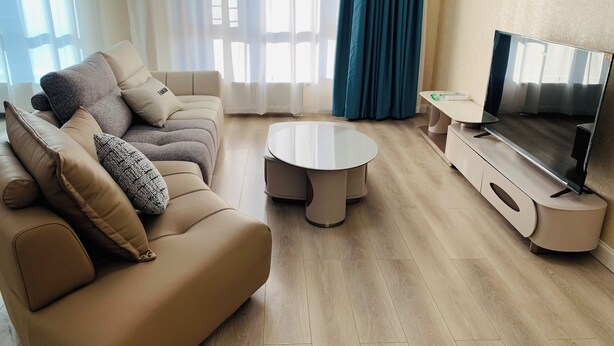Un salon moderne avec un canapé beige, une table basse ronde et un téléviseur à écran plat posé sur un meuble.
