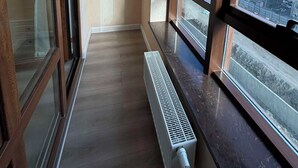Un couloir étroit, avec de grandes fenêtres d’un côté, un radiateur et une porte dotée d’un panneau de verre.
