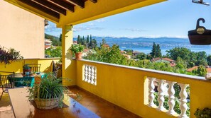 A balcony with yellow walls, white balustrades, and a view of a coastal town and mountains. - Apartman Mariana by Villas Guide (Icici)