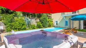 Ein Poolbereich mit Whirlpool, Liegestühlen und Sonnenschirmen.