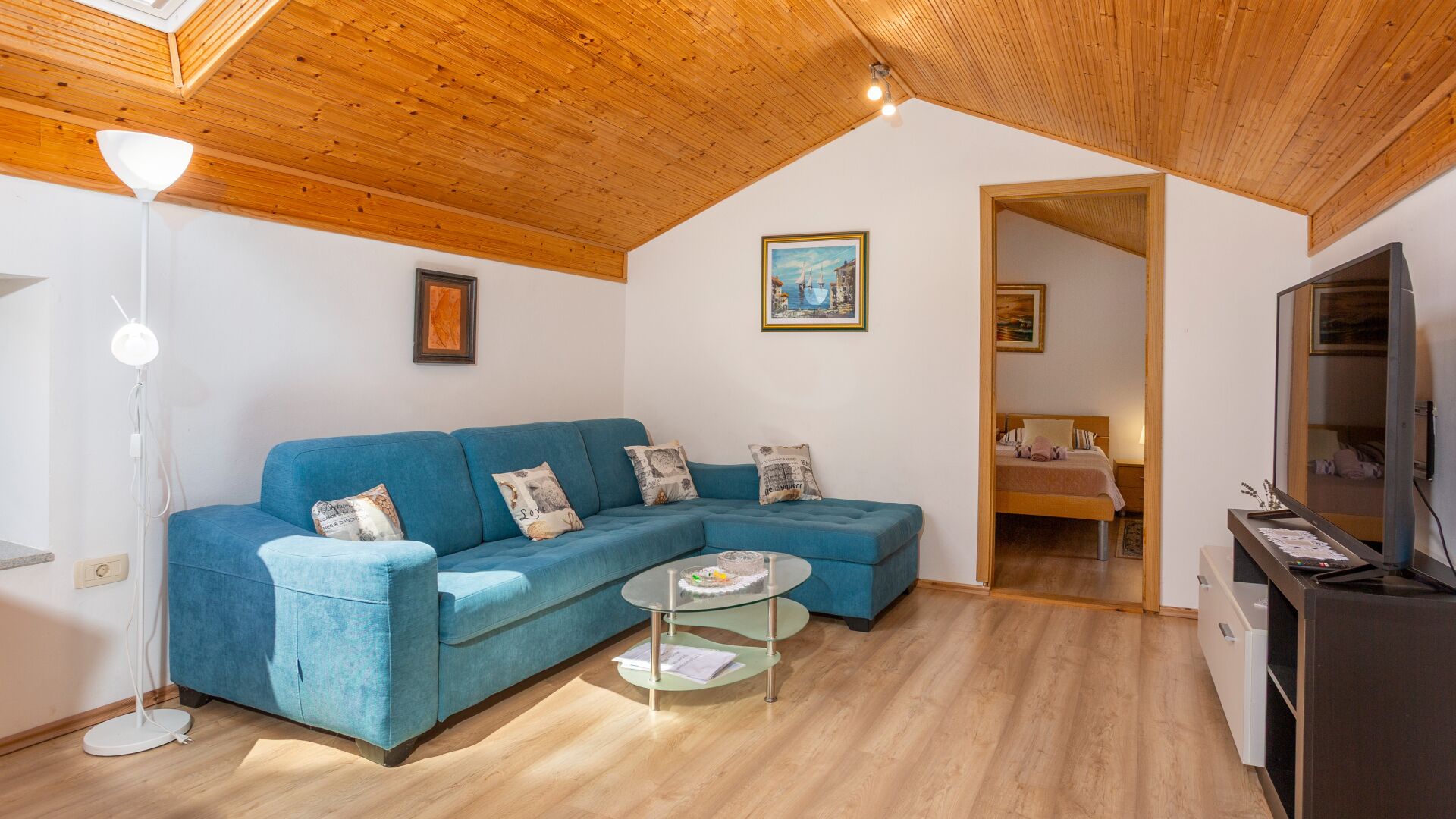 A modern living room with a blue sectional sofa, a glass coffee table, and a wooden ceiling.