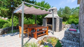 An outdoor patio with a stone oven, wooden table, and chairs under a pergola.