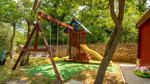 A wooden play structure with a slide and swings in a garden.
