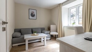 A modern living room with a grey sofa, a small white table with a plant, a white armchair, and a window with curtains. - Apartmány U Pavla (Cesky Krumlov)