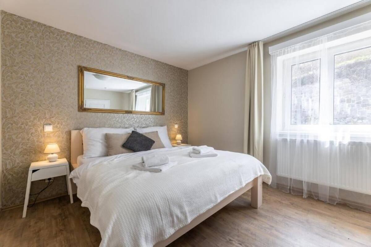 Un lit bien fait, avec du linge de lit blanc et deux oreillers, une lampe de chevet et un miroir au mur.
