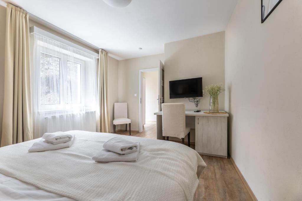 Una camera d'albergo con un letto, una scrivania, una sedia, un televisore e una finestra con tende.