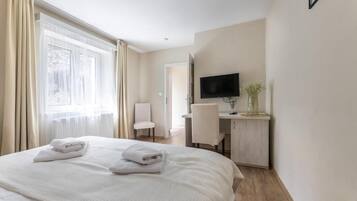 Una camera d'albergo con un letto, una scrivania, una sedia, un televisore e una finestra con tende.