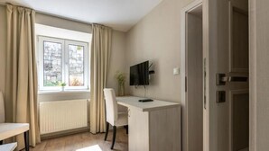 A room with a desk, chair, and a television. There is a window with curtains, a radiator, and a door. - Apartmány U Pavla (Cesky Krumlov)