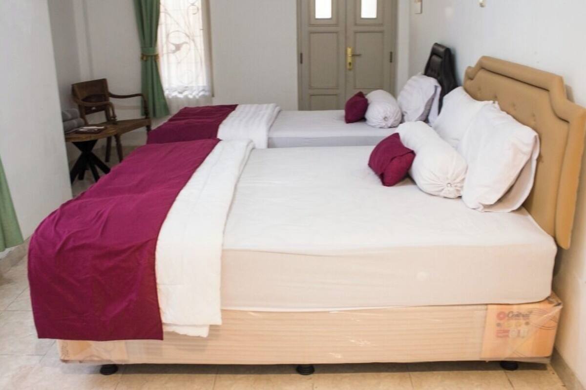 A double bed with a wooden headboard, two pillows, and a red blanket.