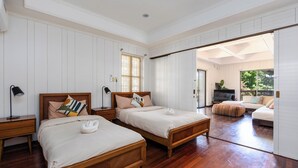 Een ruime slaapkamer met twee houten bedden, een groot raam en een schuifdeur naar een zithoek.