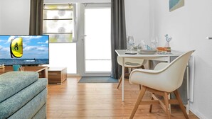 A modern living room with a television, a dining area with a table set for two, and a view of the sea through the window. - "Ankerplatz" Vacation Rental with a Terrace Between Wismar and the Island of Poel (Groß Strömkendorf)