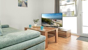 A modern living room with a wooden coffee table, a sofa, and a TV displaying a beach scene. - "Ankerplatz" Vacation Rental with a Terrace Between Wismar and the Island of Poel (Groß Strömkendorf)