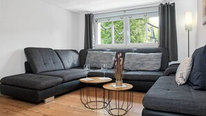 Een moderne woonkamer met een donkergrijze modulaire bank, een ronde salontafel en een groot raam met gordijnen.