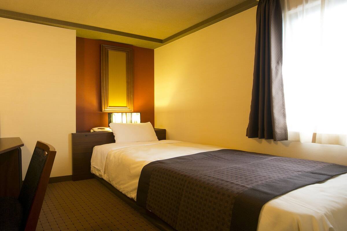 Une chambre d’hôtel équipée d’un lit, d’un bureau, d’une chaise, d’un téléphone et d’un miroir.