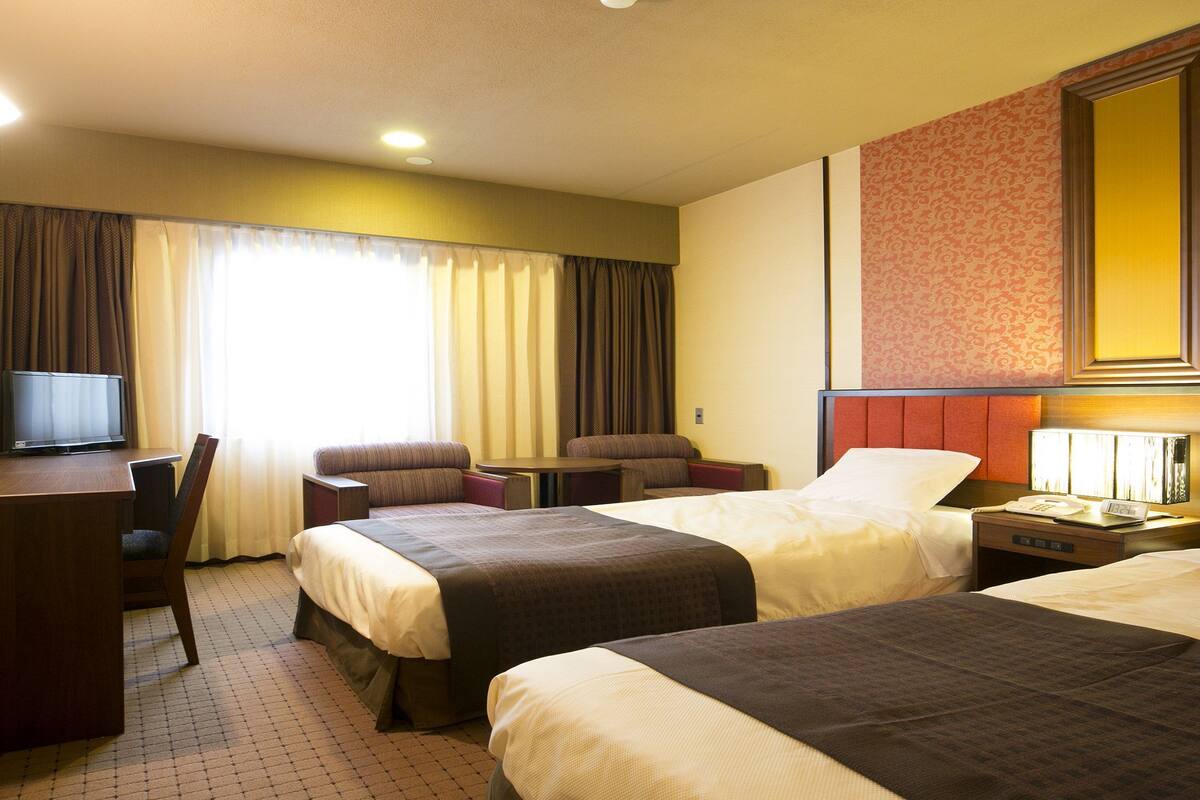 Une chambre d’hôtel avec deux lits, un bureau, une chaise, une télévision et une table de chevet avec une lampe.