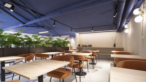 Un comedor moderno con mesas de madera y sillas anaranjadas, una barra con un florero y plantas verdes en la pared.