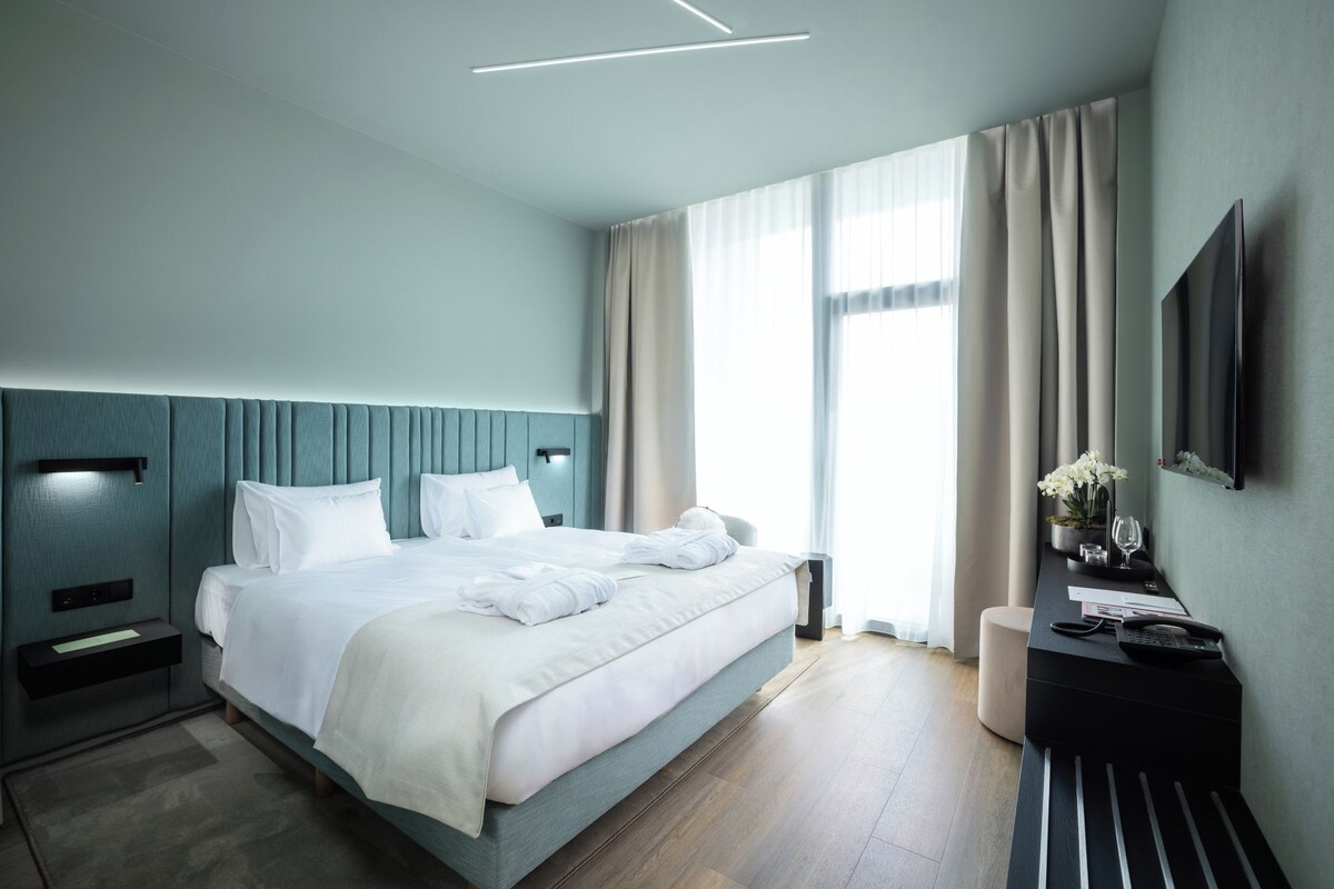 Een moderne hotelkamer met een groot bed, een bureau met een flatscreen-televisie en een raam met gordijnen.